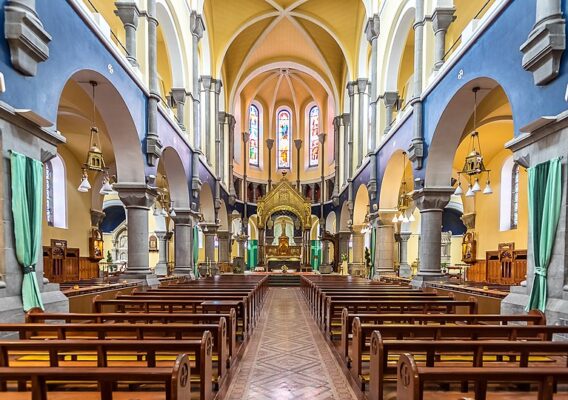 Interior view of a beautiful church featuring wooden pews, ornate altar, and colorful stained glass windows, highlighting the architectural design and serene atmosphere.