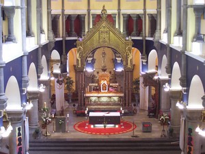 Interior view of a beautifully designed church featuring ornate altar, intricate woodwork, and colorful stained glass windows, showcasing a serene worship space with floral arrangements and decorative elements.